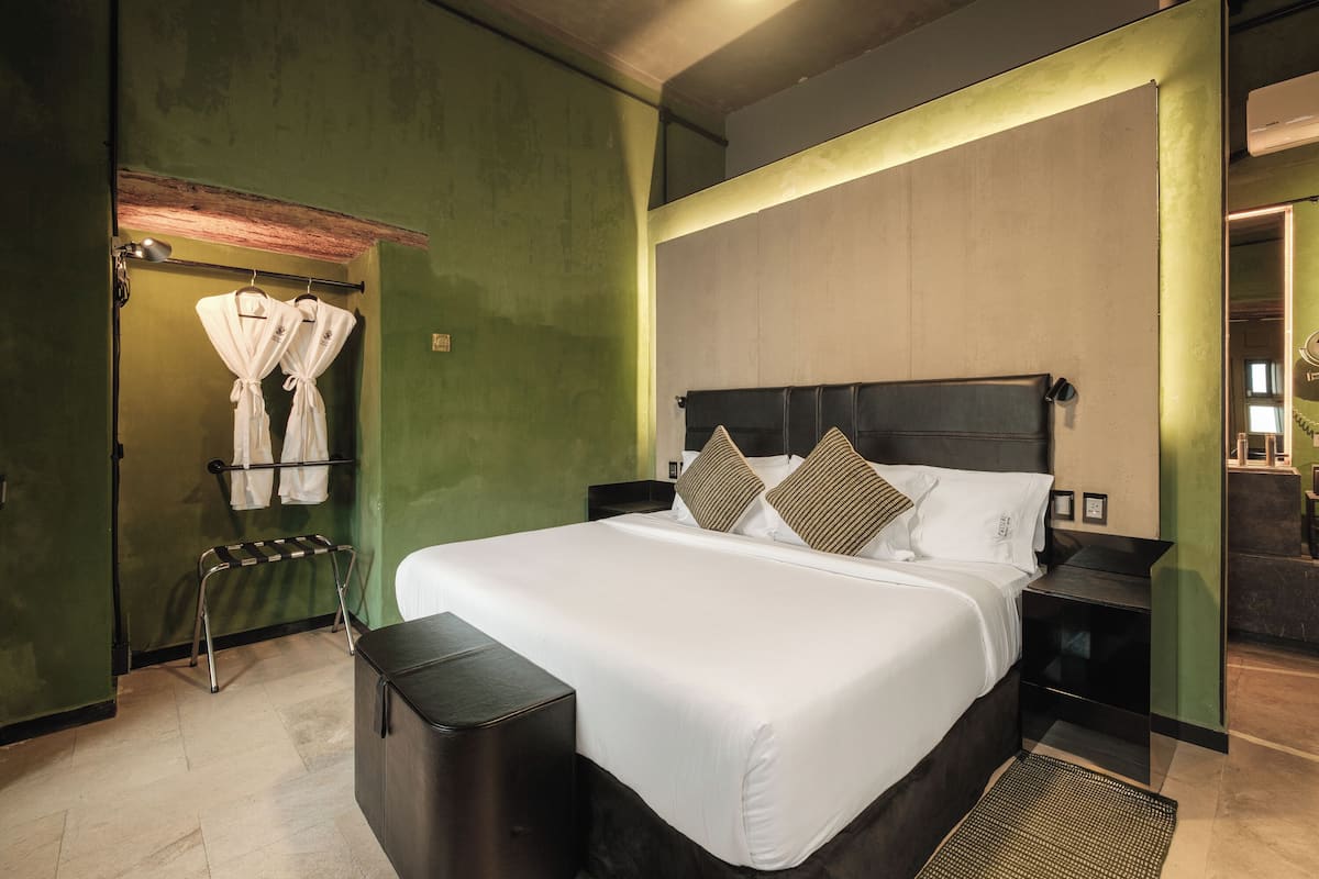 A neatly arranged hotel room with a large bed, bedside tables, a small seating area, and a wall-mounted robe rack.