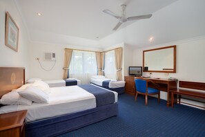 Une chambre d’hôtel avec deux lits, un bureau, une chaise, une télévision et un ventilateur de plafond.
