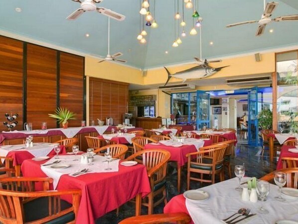 A restaurant with multiple tables, ceiling fans, and hanging lights. - Cairns Southside International (Cairns)