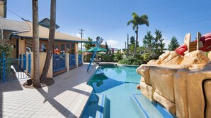 A swimming pool with a rock feature, palm trees, and a building with a tiled roof. - Cairns Southside International (Cairns)