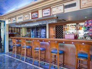 Un espace bar avec des tabourets de bar en bois et un comptoir où sont exposées différentes bouteilles.