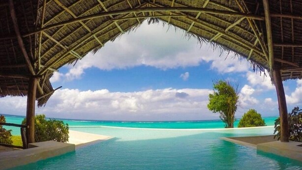 An infinity pool with a clear view of the turquoise ocean and a thatched roof structure. - Pearl Beach Resort by Sansi (Michamvi)
