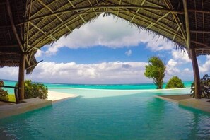 An infinity pool with a clear view of the turquoise ocean and a thatched roof structure. - Pearl Beach Resort by Sansi (Michamvi)