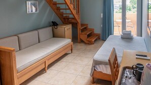 Una habitación con escalera de madera, un sofá, una mesa de comedor con sillas y vistas a través de un ventanal.