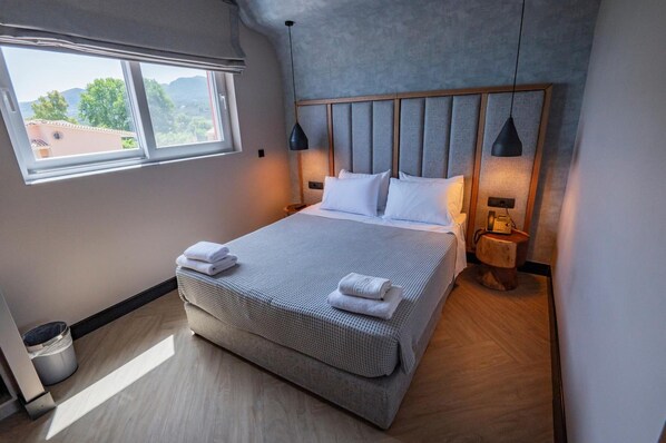Cama bem arrumada com lençóis e toalhas brancos, cabeceira de madeira e abajures laterais.
