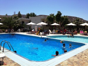 Una piscina con varias pistas, tumbonas y sombrillas.