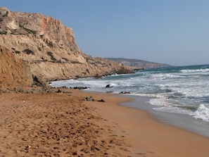 A sandy beach with rocky cliffs and waves crashing onto the shore. - Valley Village (Faistos)