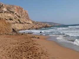Una playa arenosa con acantilados rocosos y olas rompiendo en la orilla.