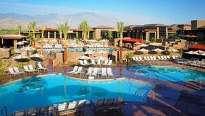 Un área de piscina en un resort con múltiples piscinas, tumbonas, sombrillas y palmeras.