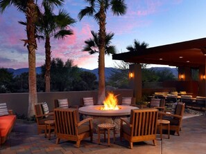 Relax in a sheltered outdoor space surrounded by palm trees and mountains, with a fire pit at its center.