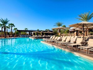 Relax by the resort pool surrounded by palm trees and shaded lounge chairs.