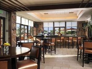 Enjoy dining in our restaurant with a central bar, round tables, and individual chairs, offering views of the outdoors.