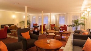 Un vestíbulo de hotel con zona de estar, chimenea y ventanas grandes con cortinas.