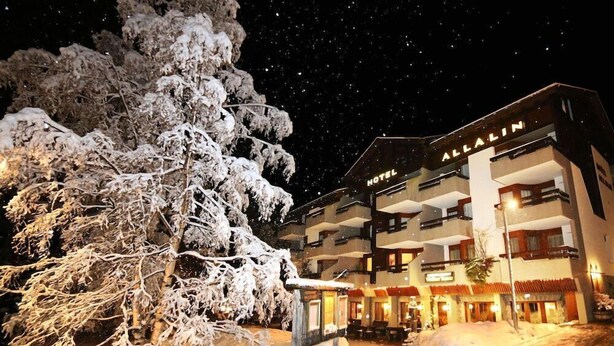 Un hotel con varios balcones y un árbol cubierto de nieve al frente.