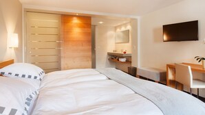 Habitación de hotel con cama, escritorio, silla, televisor y baño con espejo y lavamanos.