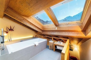 A high-ceilinged bathroom with skylights, a bathtub, and a wooden bench. - Allalin Relais Du Silence Hotel (Saas-Fee)