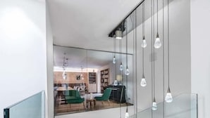 A modern interior with a glass staircase, hanging light fixtures, and a view into a dining area with green chairs and a wooden table. - Impuls Hotel Tirol (Bad Hofgastein)