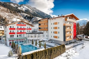 A hotel with multiple floors, a swimming pool, and a mountainous backdrop. - Impuls Hotel Tirol (Bad Hofgastein)