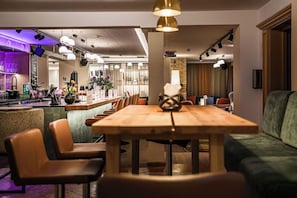 A modern interior with a wooden dining table, leather chairs, and a green sofa. - Impuls Hotel Tirol (Bad Hofgastein)