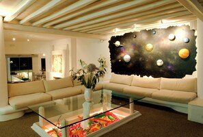 Ein modernes Wohnzimmer mit Glastisch, beiger Couch und einer Wandmalerei von Planeten.