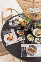 Uma mesa de jantar redonda com diversos pratos, copos e uma cadeira de vime.