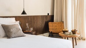 Une chambre d’hôtel moderne avec un grand lit, une tête de lit en bois, une petite table avec une lampe et une chaise.