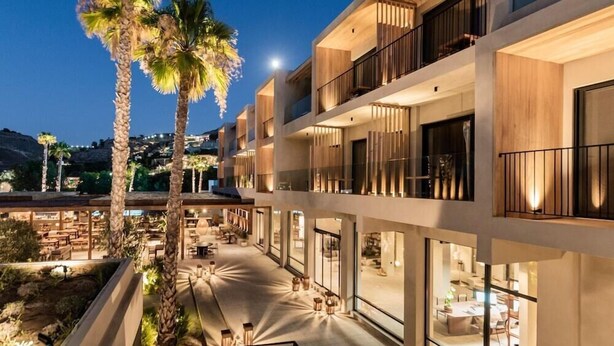 Un hôtel à plusieurs étages doté de balcons, une cour intérieure agrémentée de palmiers et des espaces de détente en plein air.