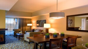 A hotel room with a living area, dining table, and chairs. There are two lamps, a sofa, and a coffee table.