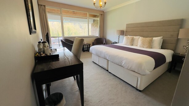 Habitación de hotel con cama, mesita de noche, escritorio, silla y vistas al exterior a través de amplias ventanas.