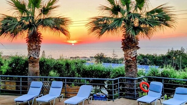Zonsondergang met palmbomen en ligstoelen op een balkon.