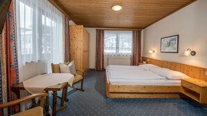 Una habitación con techo de madera, una cama, un escritorio y una silla. Hay una ventana con cortinas y un cuadro en la pared.