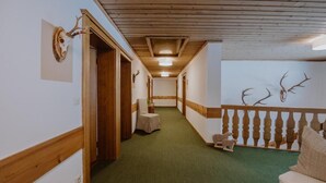 Un pasillo con paneles de madera, alfombra verde y decoración de cuernos en las paredes.