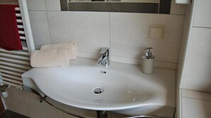 Un baño con un lavamanos blanco, un espejo encima y una toalla roja colgada en un radiador.