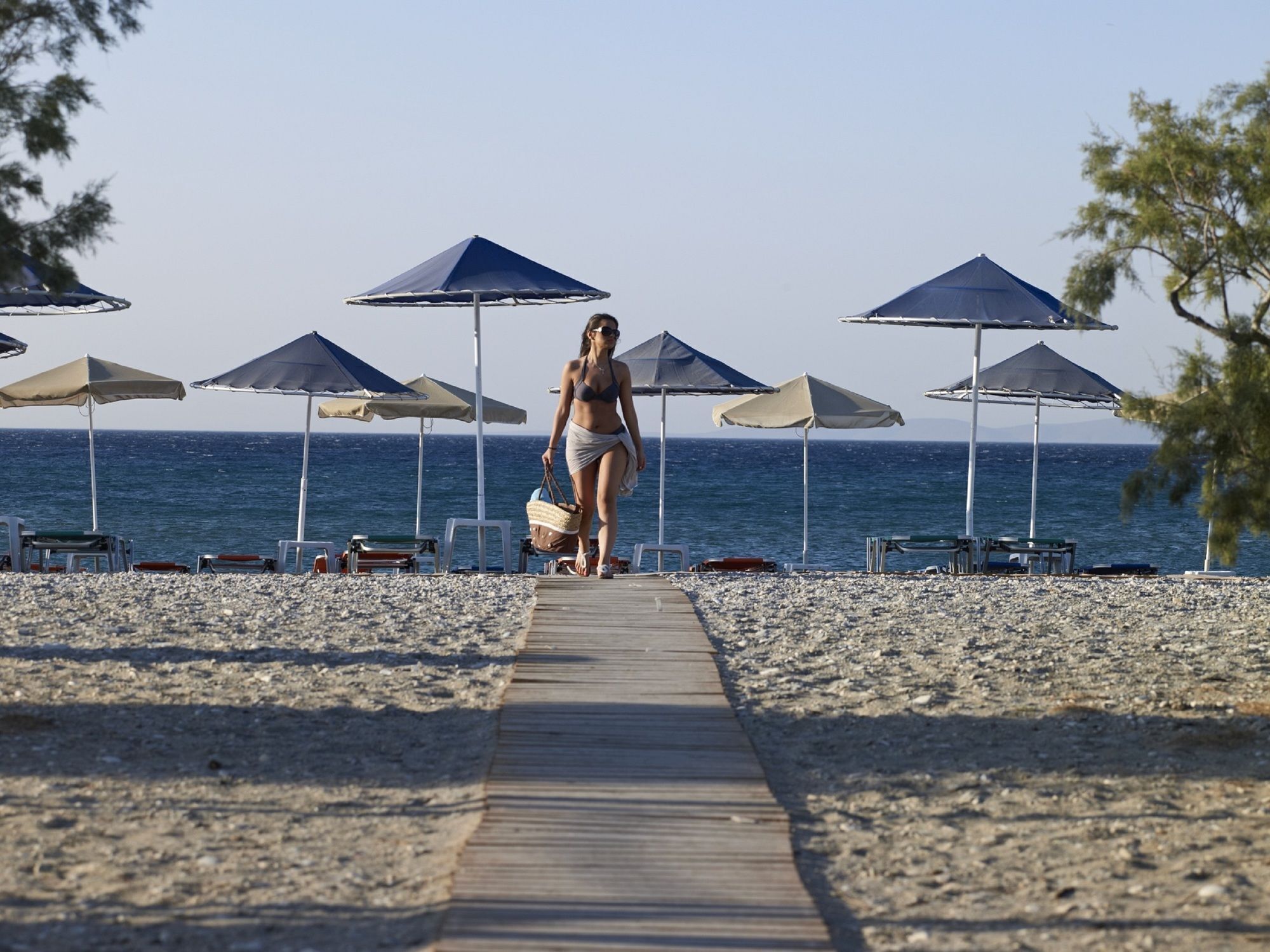 A beach with a wooden walkway leading to the sea, surrounded by umbrellas and beach chairs.