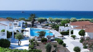 Un resort con piscina central, zonas de descanso y vistas al mar.