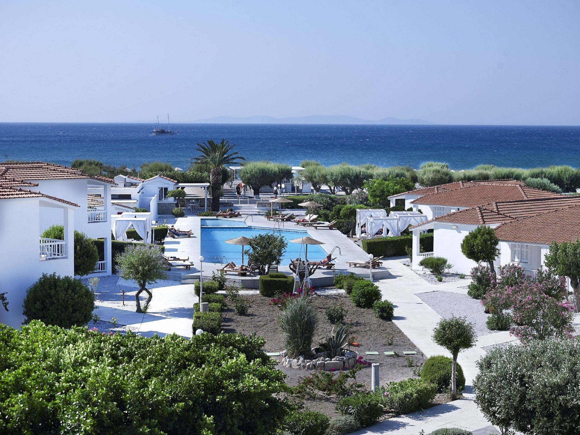 A resort with a swimming pool, white buildings, and a view of the sea.