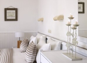 A bedroom with a white bed, striped pillows, a bedside table with a candle holder, and a framed picture on the wall. - Fito Hotel (Samos)