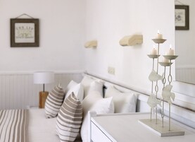 Un dormitorio con cama blanca, almohadas a rayas, una mesita de noche con un candelabro y un cuadro en la pared.