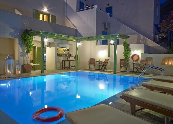A swimming pool with lounge chairs and a bar area. - Markos Studios (Santorini)