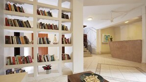Un vestíbulo amplio con una gran estantería llena de libros, un mostrador de recepción y una escalera que sube a los pisos superiores.