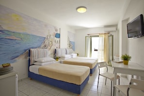 A room with two beds, a desk, a chair, a TV, and a painting of a coastal scene. - Markos Studios (Santorini)