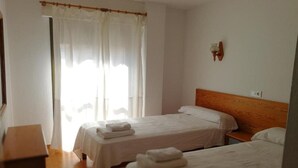 Una habitación con dos camas individuales, cabecero de madera, una mesita pequeña y una ventana con cortinas.