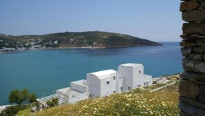 Vista costera con edificios blancos, un muro de piedra y un mar azul cristalino.