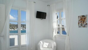 Una habitación con cama, una silla, un televisor en la pared y un ventanal con cortinas.