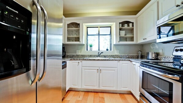 A modern kitchen with white cabinets, stainless steel appliances, and a window above the sink.