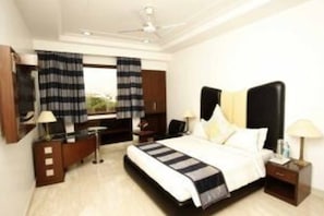 A hotel room with a bed, bedside tables, a desk, a chair, a wardrobe, and a window with curtains. - Star Grand Villa (New Delhi)