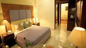 A hotel room with a large bed, bedside tables, a nightstand, a lamp, and a glass coffee table. - Star Grand Villa (New Delhi)