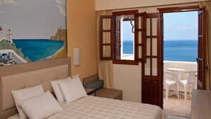 A hotel room with a bed, a painting of a coastal scene, a balcony with a view of the sea, and a table with chairs. - Amopi Bay Hotel (Karpathos)