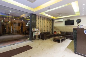 A modern lobby with a glass entrance, a seating area with sofas, a coffee table, and a reception desk. - Kingston Park (New Delhi)