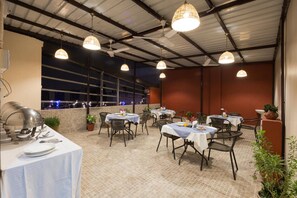 An outdoor dining area with round tables, chairs, and hanging pendant lights. - Kingston Park (New Delhi)